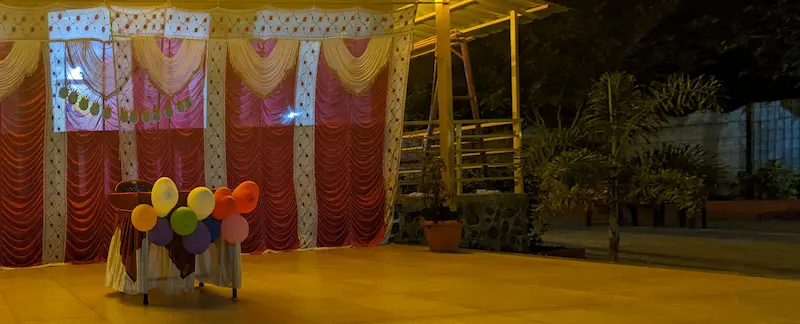 Image of a stage with warm dramatic lighting. A table with balloons is in the foreground.