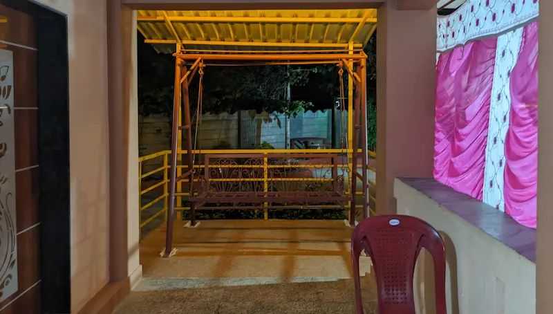 A dark red metal swing with a yellow metal roof above it